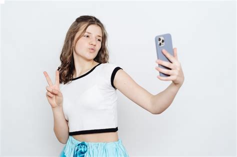 Adolescente Chica Alegre Tomando Selfie Con Teléfono Mientras Posa En Blanco Foto Gratis