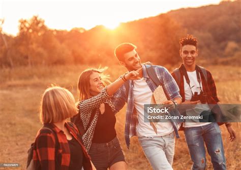 Group Of Four Friends Hiking Through Countryside Together At Sunset