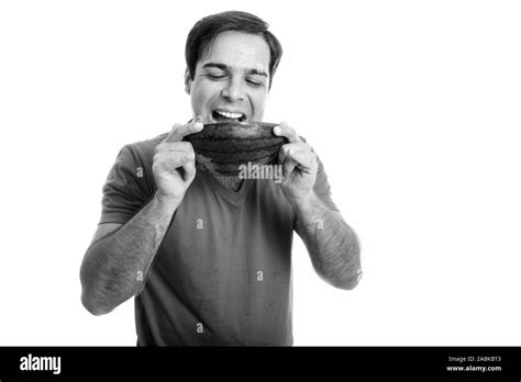 Studio shot of young happy Persian man smiling while eating and looking
