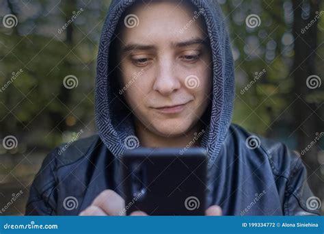 Concept A Man In A Leather Jacket With A Hood Looks At The Phone And