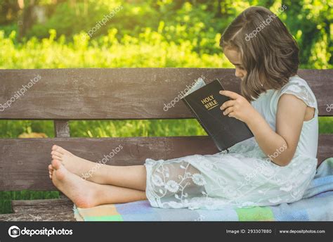 reading the holy bible in outdoors christian girl holds bible in her hands sitting on a bench