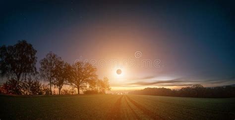 Total Solar Eclipse During Sunrise Over A Green Field And Trees Along