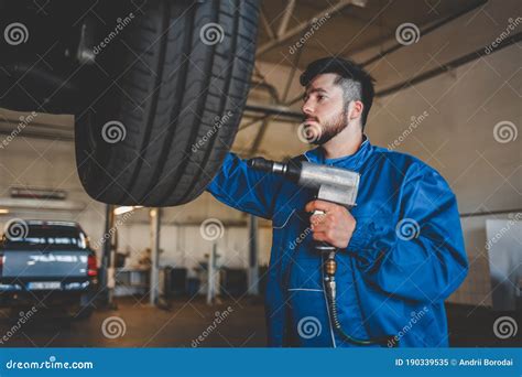 Auto Mechanic With Wrench Stands Near A Car On A Lift Car Repairman In