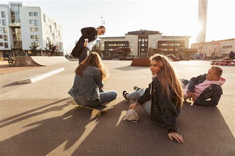 Portrait Of Smiling Teenage Girl Hanging Out With Friends At Skateboard Park During Sunny Day
