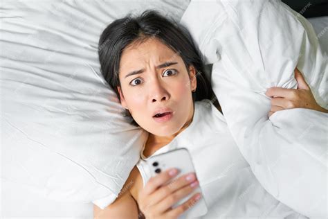 free photo portrait of asian girl wakes up in morning looks at mobile phone with shocked face