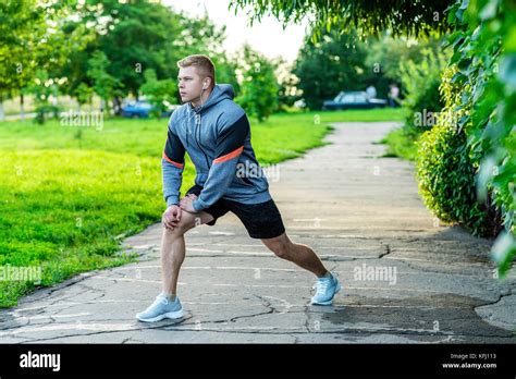 A Male Athlete Warms Up Before Jogging In The Park Listens To Music On