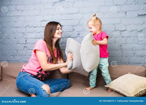 Mom And Daughter Play On The Couch With Pillows Fight Dressed In Bright Stylish Clothes In A