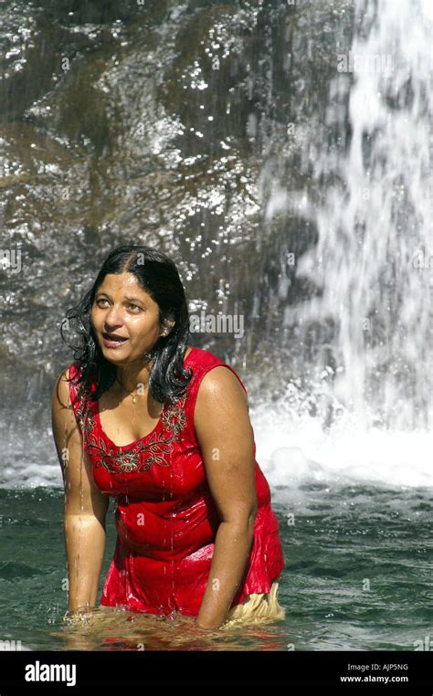 korpulente junge indische frau baden im freien unter wasserfall gekleidet im roten trikot