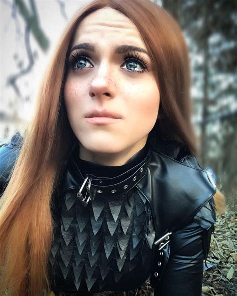 a woman with long red hair and black leather outfit posing for a photo in the woods