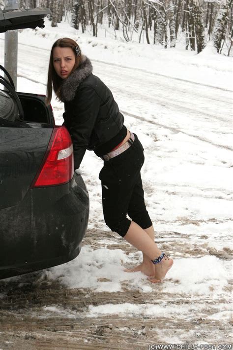 A Woman Standing Next To A Car In The Snow With Her Foot On The Trunk