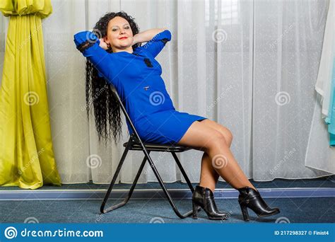 Curly Brunette Woman In Blue Sits On A Chair With Her Head Thrown Back Stock Image Image Of