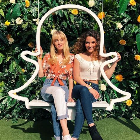 Two Women Sitting On A Swing In Front Of A Flower Wall
