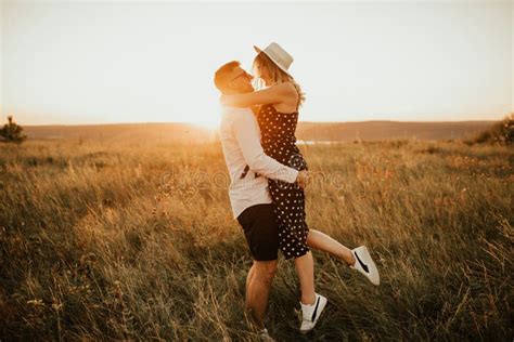 A Man With A Woman In A Hat Hug And Kiss In The Tall Grass In The Meadow Stock Image Image Of