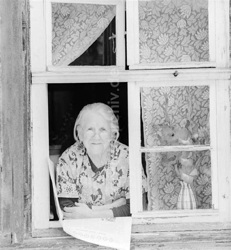 DDR Fotoarchiv Quedlinburg Ältere Frau mit Kittelschürze und Brille schaut aus einem Fenster