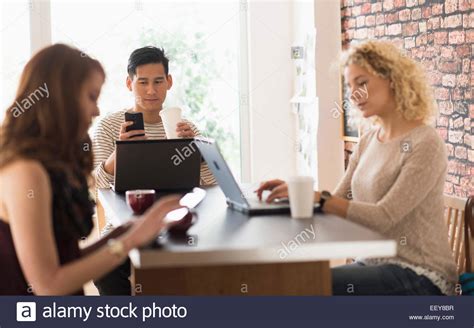 Friends Sitting In Cafe Using Laptops And Digital Tablet Stock Photo