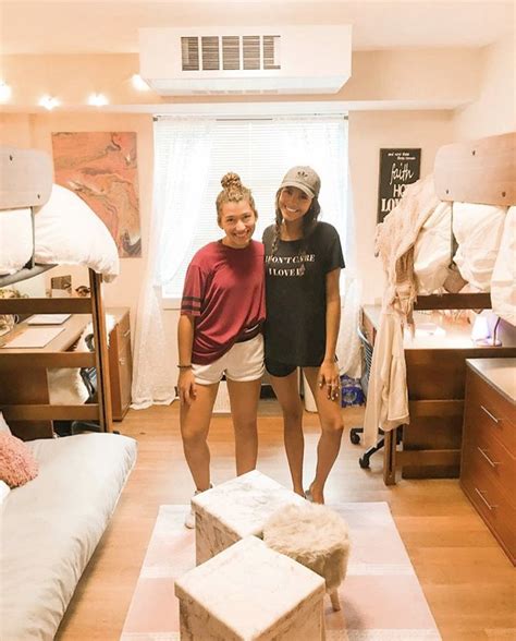 Two Women Standing In A Dorm Room With Bunk Beds And Other Items On The