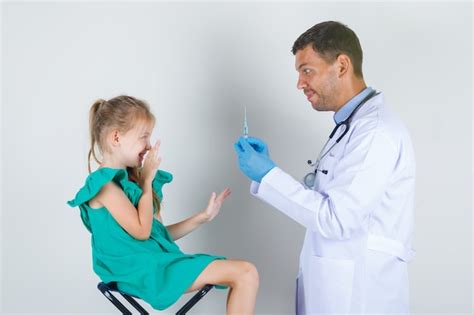 Médico Homem De Uniforme Branco Luvas Segurando Uma Seringa Enquanto Criança Olhando Com Medo