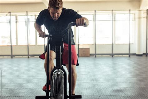 Fit Young Man Using Air Bike For Cardio Workout At Gym Del