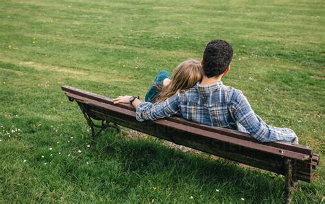 Back View Of Young Couple Sitting On Bench On A Meadow Stock Photo