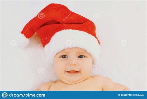 Christmas Portrait Of Happy Cute Baby In Red Santa Hat Lying On White