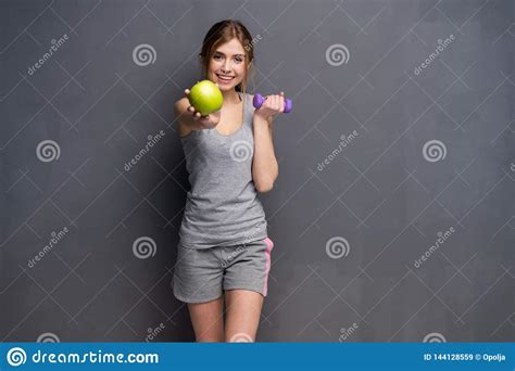Sporty Fit Woman Holding Dumbbells Weights In One And Apple Fruit In
