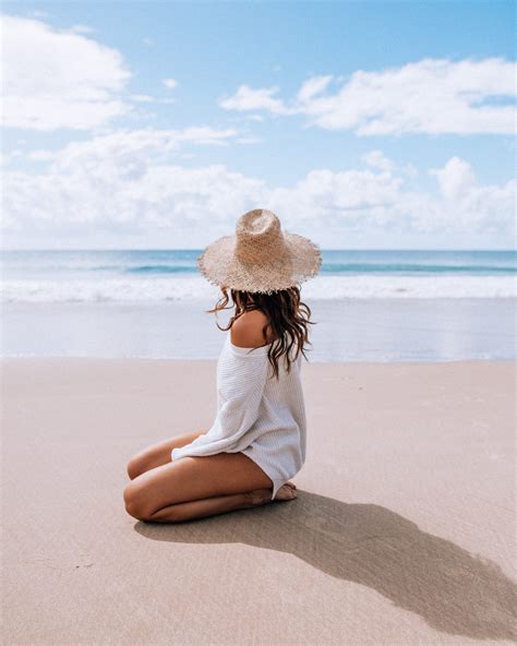 A Woman Sitting On The Beach Wearing A Hat