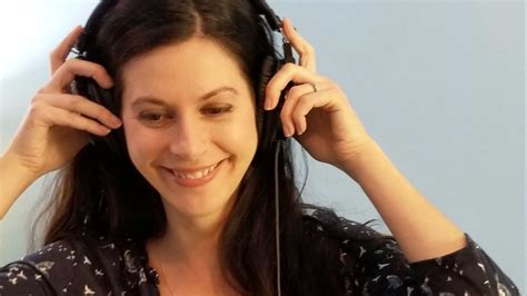 A Woman Is Listening To Music With Headphones On Her Ears And Smiling At The Camera