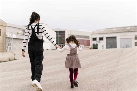 Mother And Daughter Holding Hands While Walking On Street Stock Photo