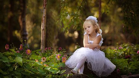 Cute Little Girl Is Sitting On Rock Wearing White Dress In Blur