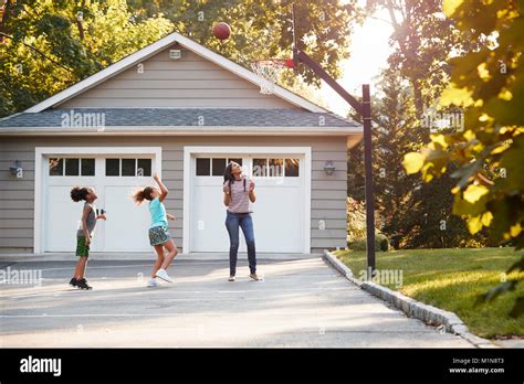 Mother And Children Playing Basketball On Driveway At Home Stock Photo