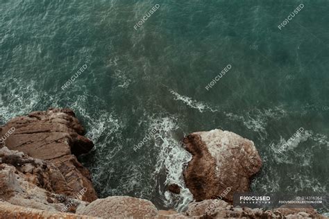 Aerial View Of Sea Waves Hitting Rocky Cliff With Splash And Foam On