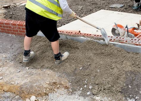 Groundworker Placing Semi Dry Concrete Around Concrete Edging Kerb