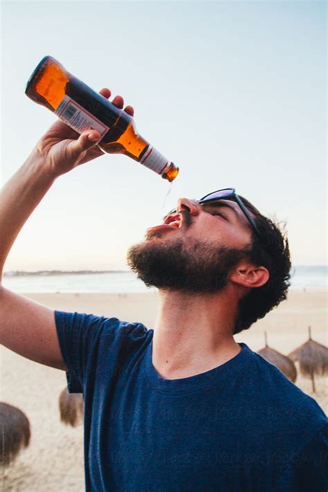 Man Drinking The Last Drop Of His Bottle Of Beer On A Beach Bar By