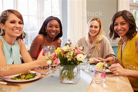 Female Friends At Home Sitting Around Table For Dinner Party Stock