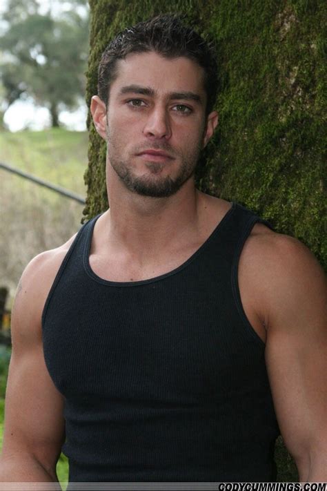 A Man Standing Next To A Tree In Front Of A Green Wall Wearing A Black