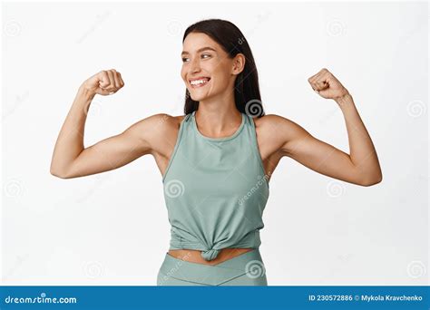 Happy Brunette Sportswoman Flexing Biceps Smiling And Looking Aside
