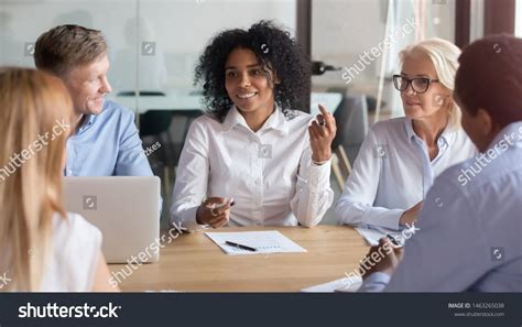 Diverse Smiling Colleagues Sit At Office Desk Negotiate Discuss Project