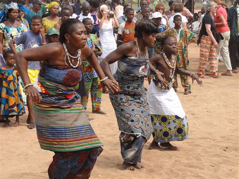 Two Women Dancing In Front Of A Large Group Of People On A Dirt Field