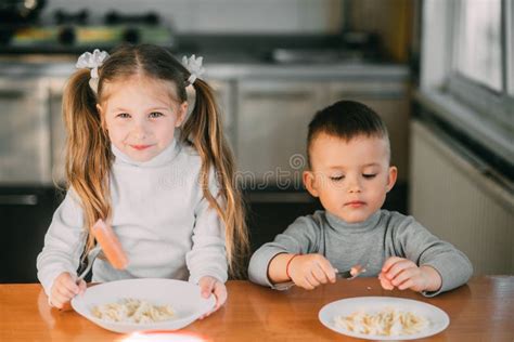 Boy And Girl Children In The Kitchen Eating Sausages With Pasta Is Very