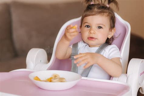 Portrait Of Happy Young Baby Girl In High Chair Eating Exotic Fruits