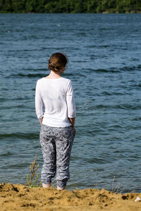 Young Girl Stands On The River Bank And Looks At The Water Standing