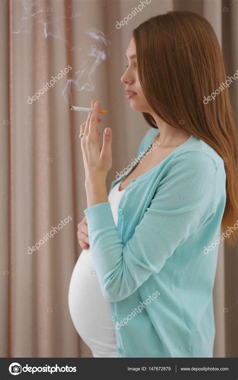 Mujer embarazada fumando cigarrillo en el fondo cortinas fotografía de