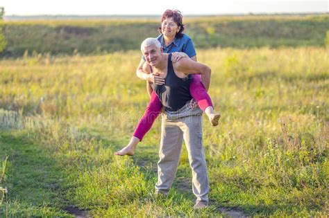 Happy And Mature Couple In Love Walk Along The Sandy Bank Of The River On A Summer Sunny Day