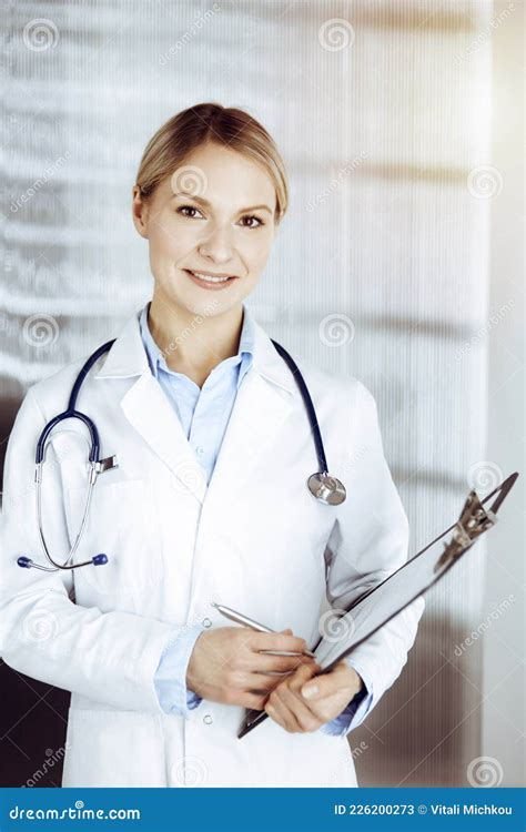 Friendly Female Doctor Standing In Sunny Clinic Portrait Of Cheerful
