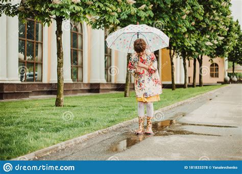 A Beautiful Girl In A Bright Rain Jacket Walks Under An