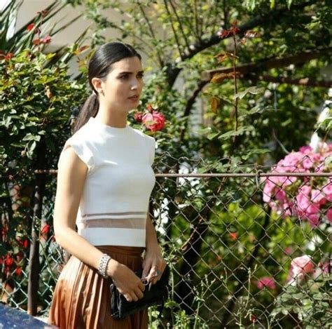 A Woman In A White Top And Brown Skirt Standing Next To A Fence With