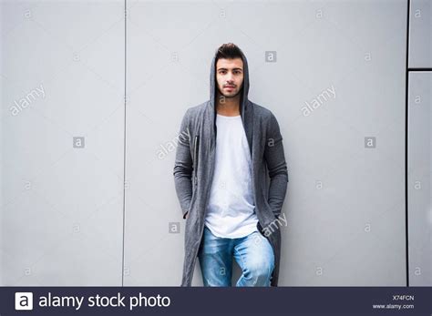 Young Man Leaning Against Grey Wall With Hands In Pocket Stock Photo