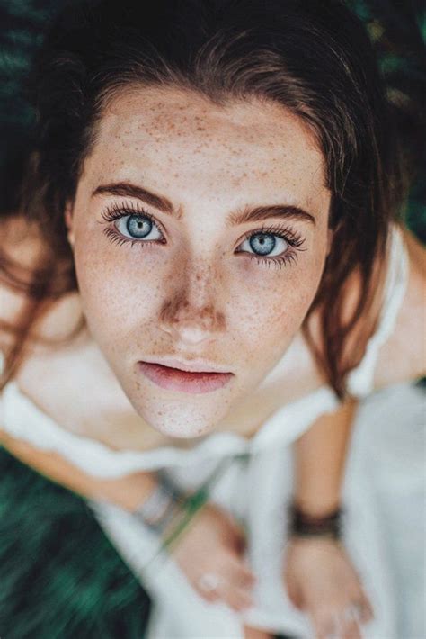 A Woman With Freckled Hair And Blue Eyes Is Laying On The Green Grass