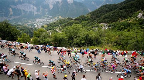 A Large Group Of Bicyclists Riding Down A Road In Front Of Mountains