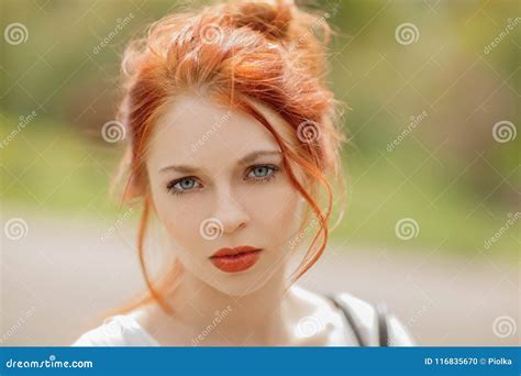 Beautiful Young Woman With Red Hair Outside In A Park In The Sunlight Looking Into The Camera